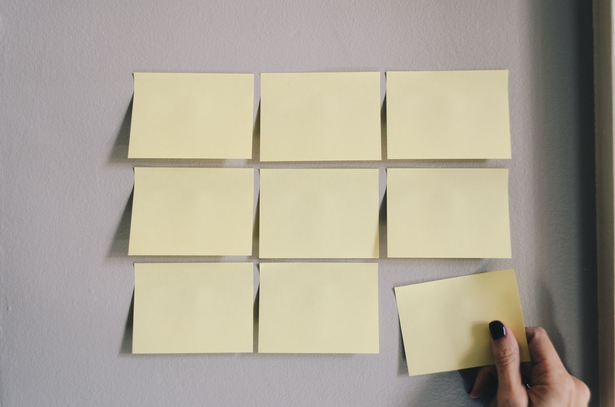A person holding up yellow sticky notes on a wall.