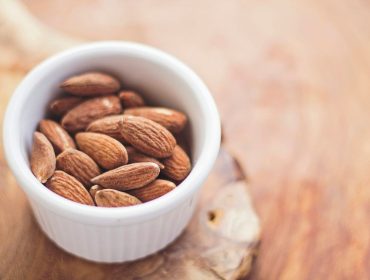 Almonds in a white bowl on a wooden table.